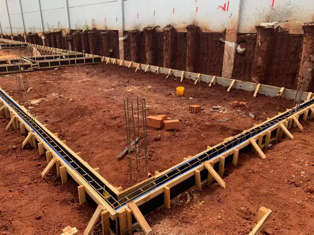 Fundação de baldrame com formas de madeira e ferragem em terreno de terra vermelha, obra