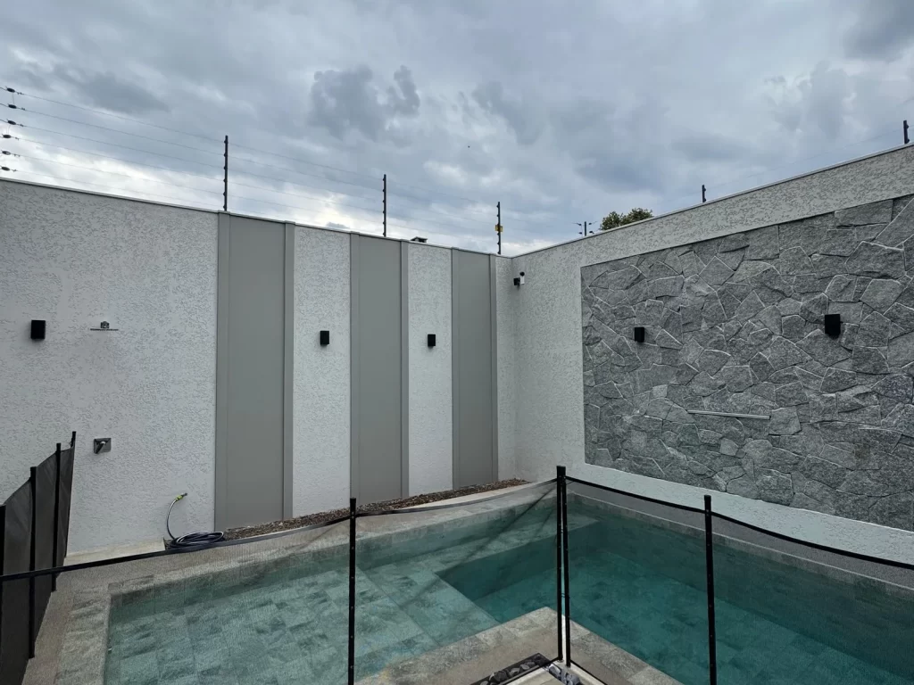 Área de lazer entregue com piscina, cerca de vidro e parede revestida em pedra cinza