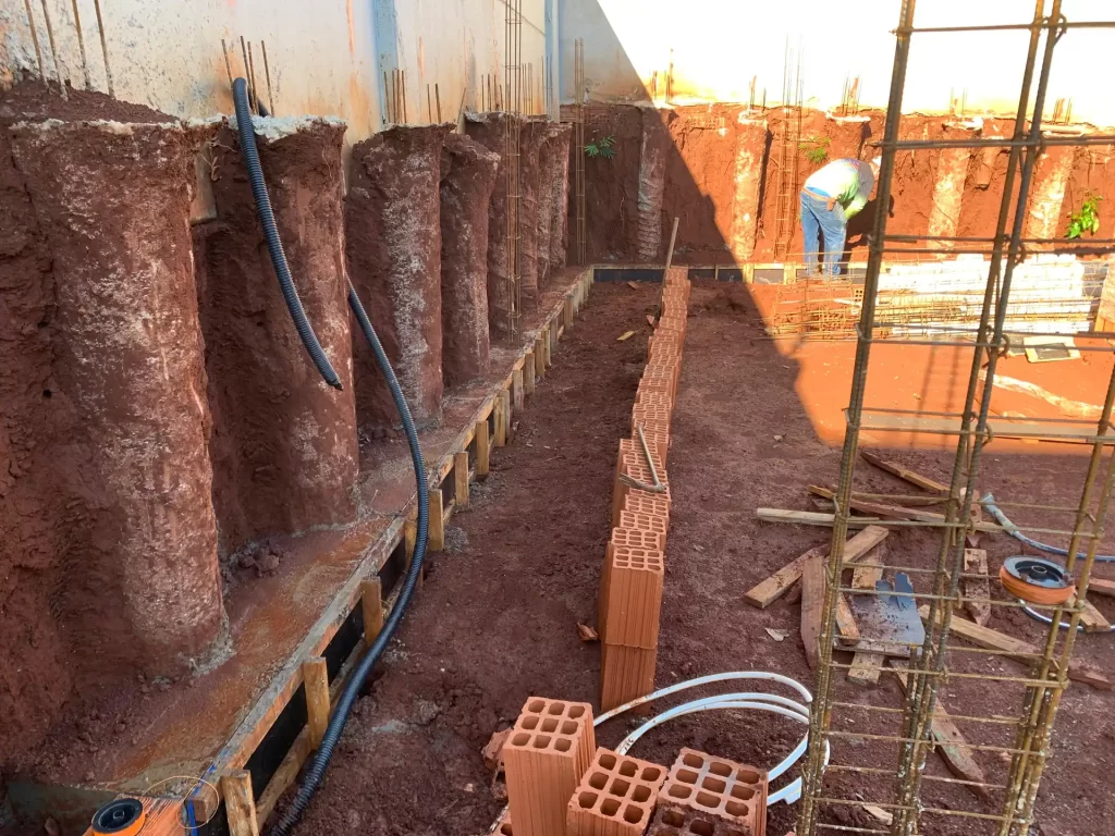 Muro de arrimo com tubulões, ferragem e tubulação em escavação de terra vermelha, obra