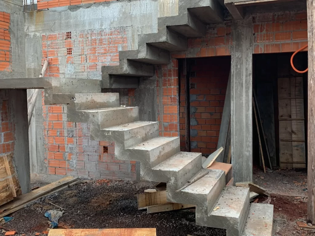 Escada de concreto aparente em balanço entre paredes de tijolo, obra em estrutura