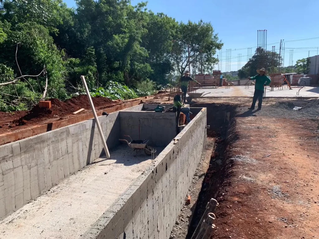 Muro de arrimo de concreto ao longo de terreno escavado, operários trabalhando ao fundo