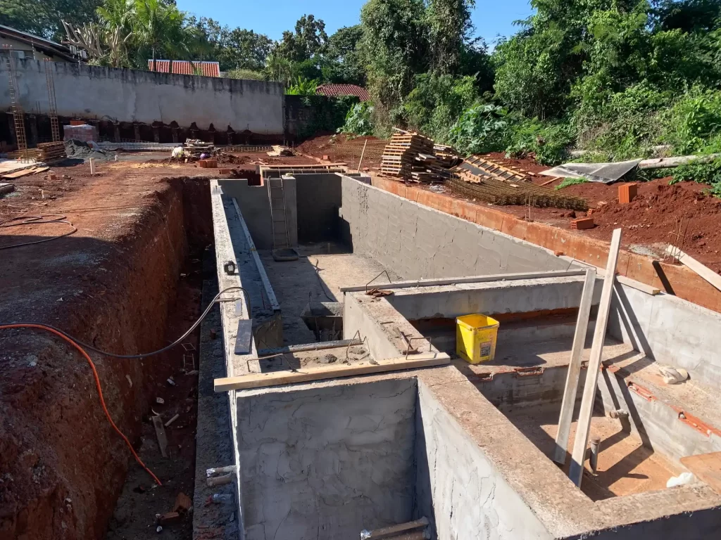 Piscina de concreto em escavação com formas de madeira, vista lateral em terreno arborizado, obra
