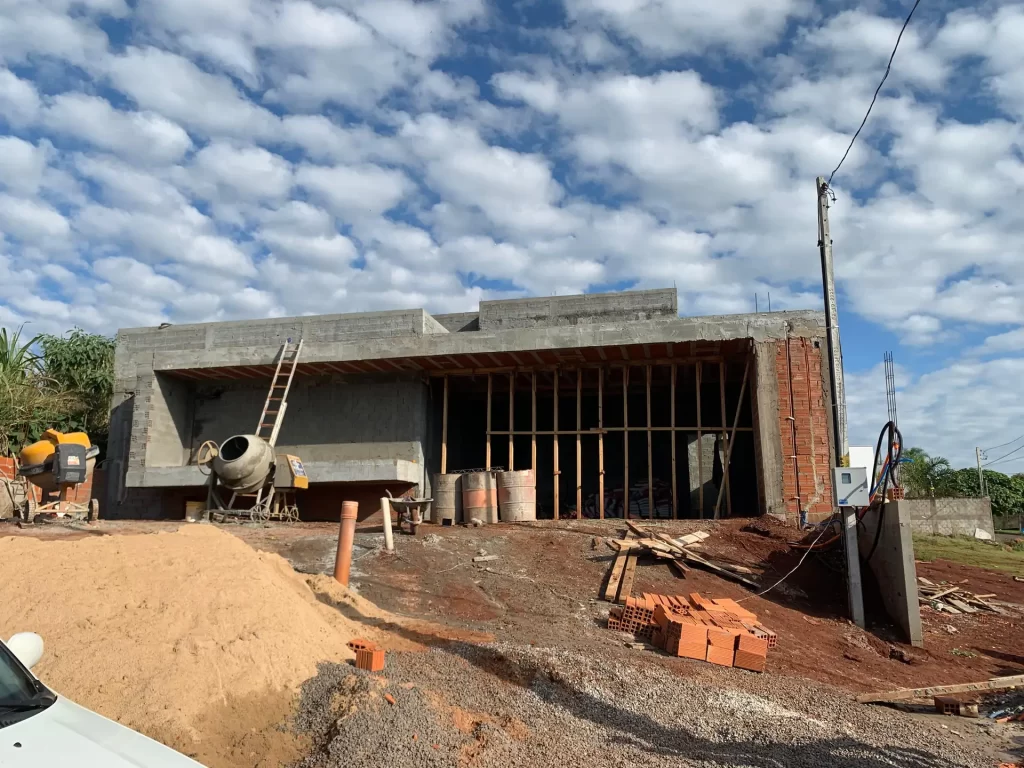 Residência de concreto aparente em estrutura com betoneira e aterro em primeiro plano, obra