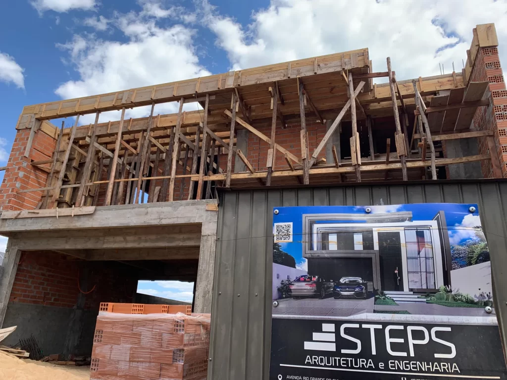 Estrutura de madeira para telhado sobre sobrado em obra ao lado de placa STEPS Arquitetura e Engenharia