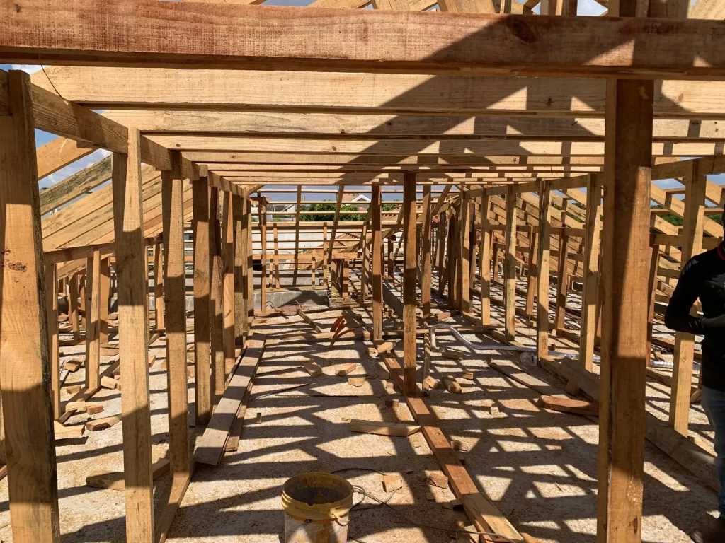 Vista interna de estrutura de madeira de telhado em construção, com vigas e caibros alinhados