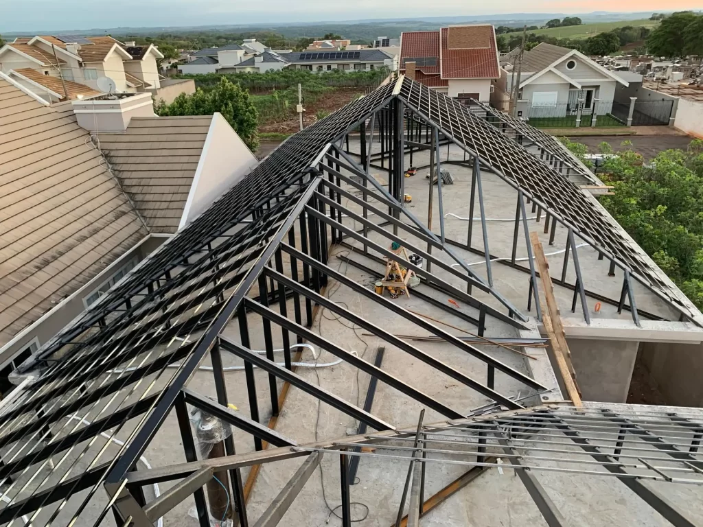Vista aérea de estrutura metálica preta de telhado em residência em obra, bairro ao fundo