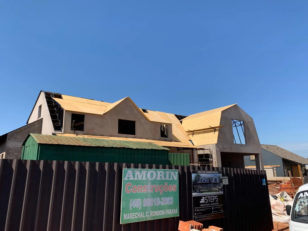 Sobrado em estrutura com cobertura de OSB atrás de tapume com placas Amorin Construções e STEPS