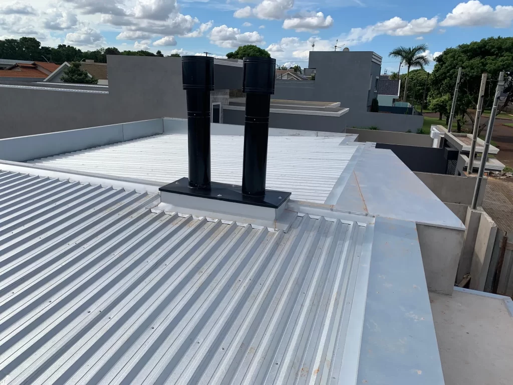Cobertura metálica branca com dutos pretos vista do alto de residência em obra