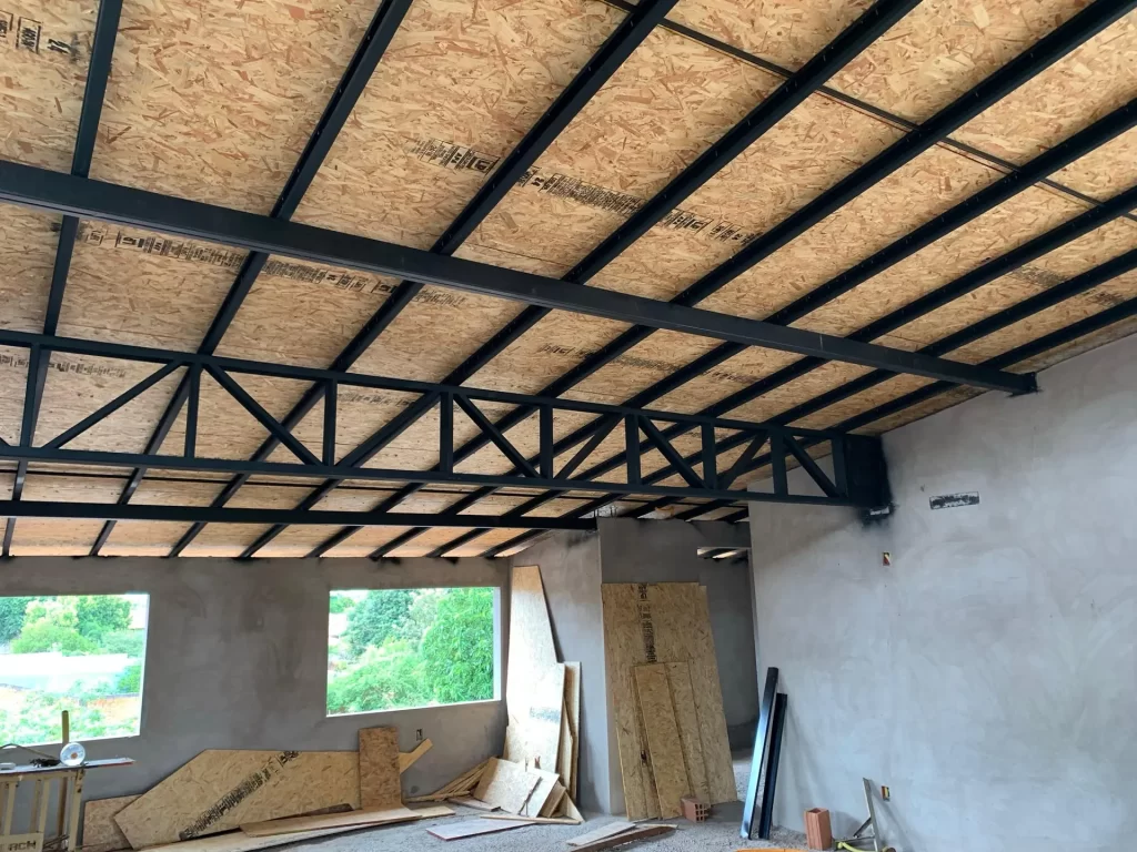 Interior com estrutura metálica de telhado e forro de OSB sobre paredes rebocadas, obra