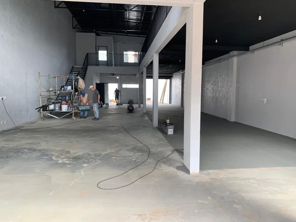 Interior bruto de salão comercial com mezanino e estrutura metálica, operários no contrapiso