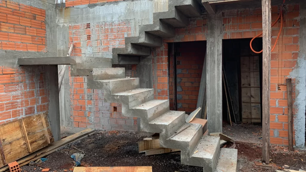 Escada de concreto aparente em balanço entre paredes de tijolo, interior bruto em obra