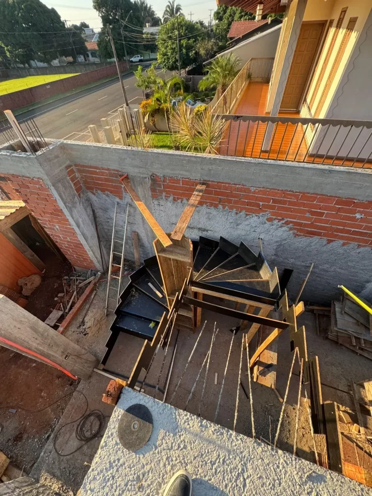 Vista superior de escada caracol metálica em poço de concreto e tijolo, residência em obra