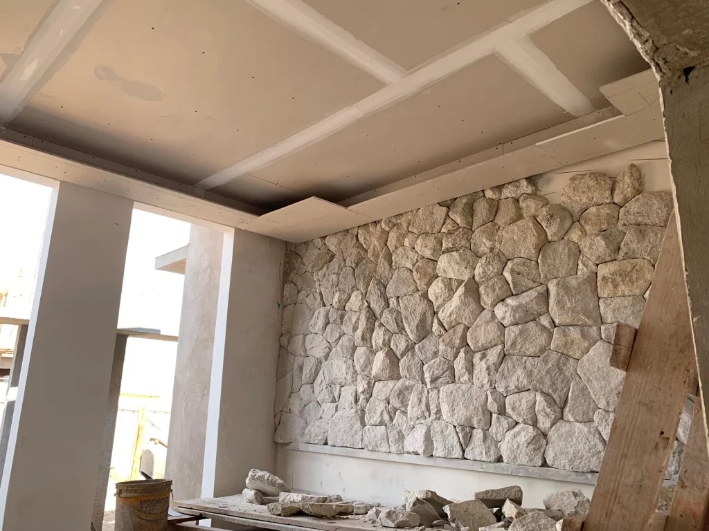 Parede de pedra natural e forro de gesso em interior em acabamento, obra