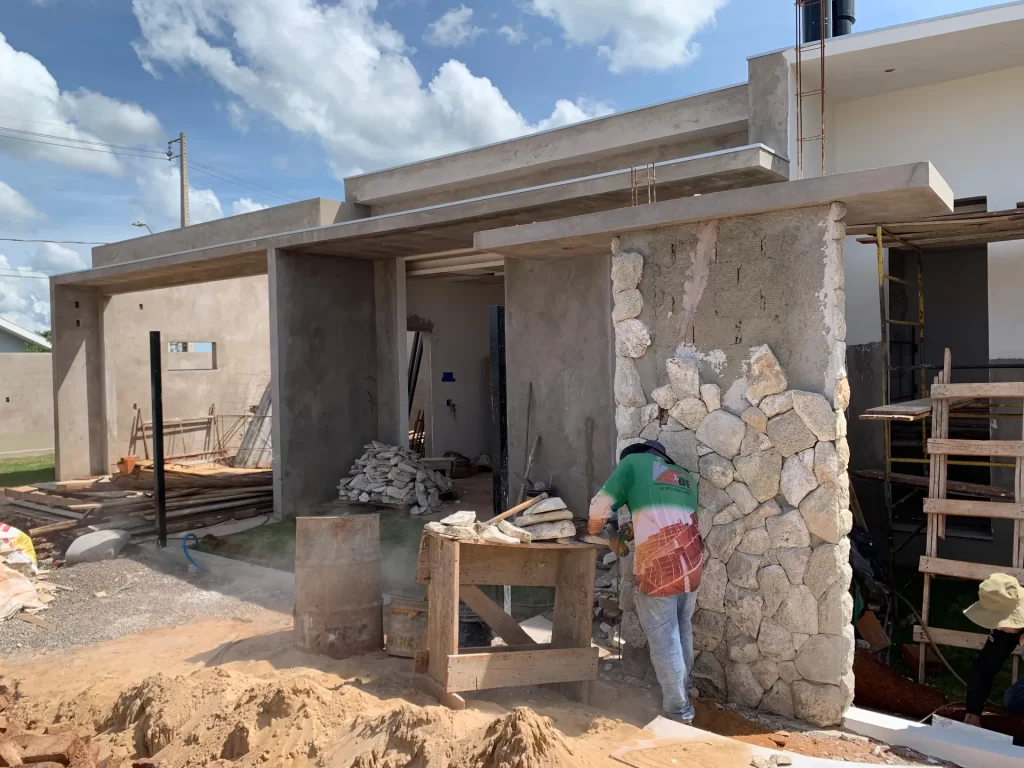 Operário assentando revestimento de pedra em pilar de fachada de residência em obra
