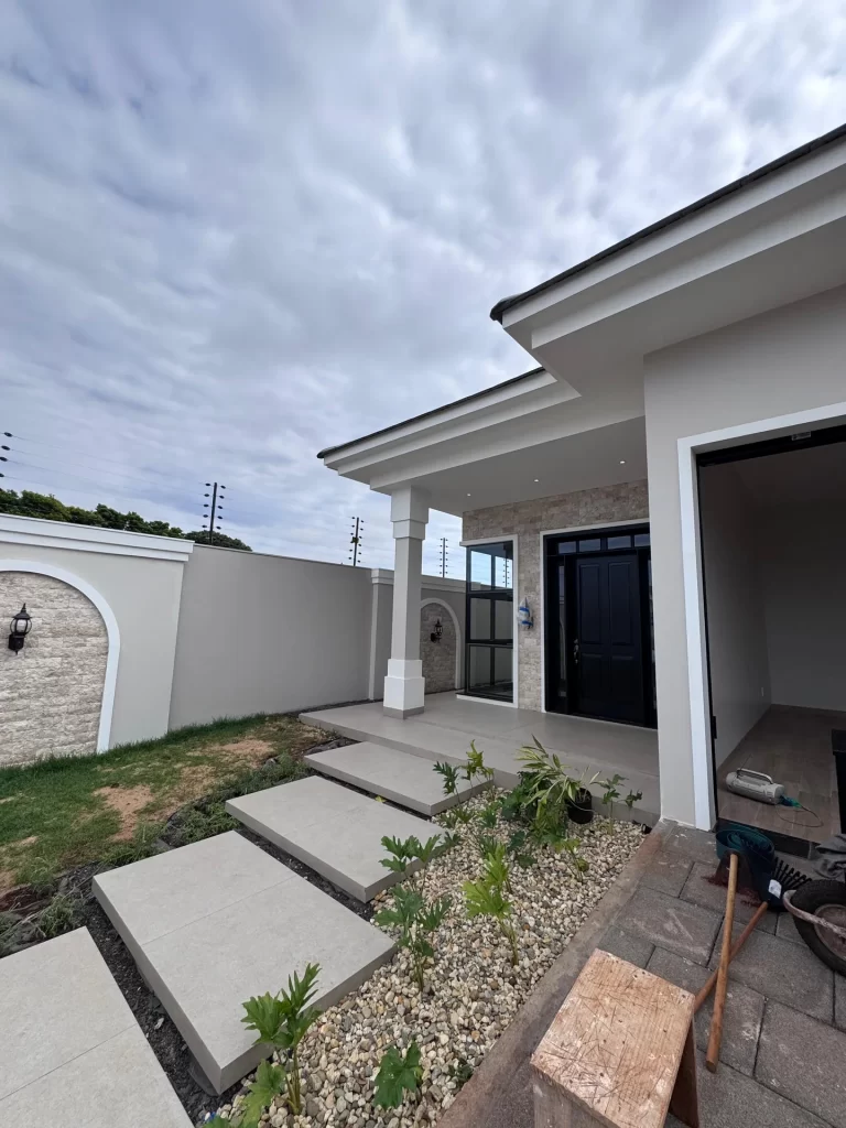 Entrada de residência com varanda, porta preta, jardim de pedras e paisagismo