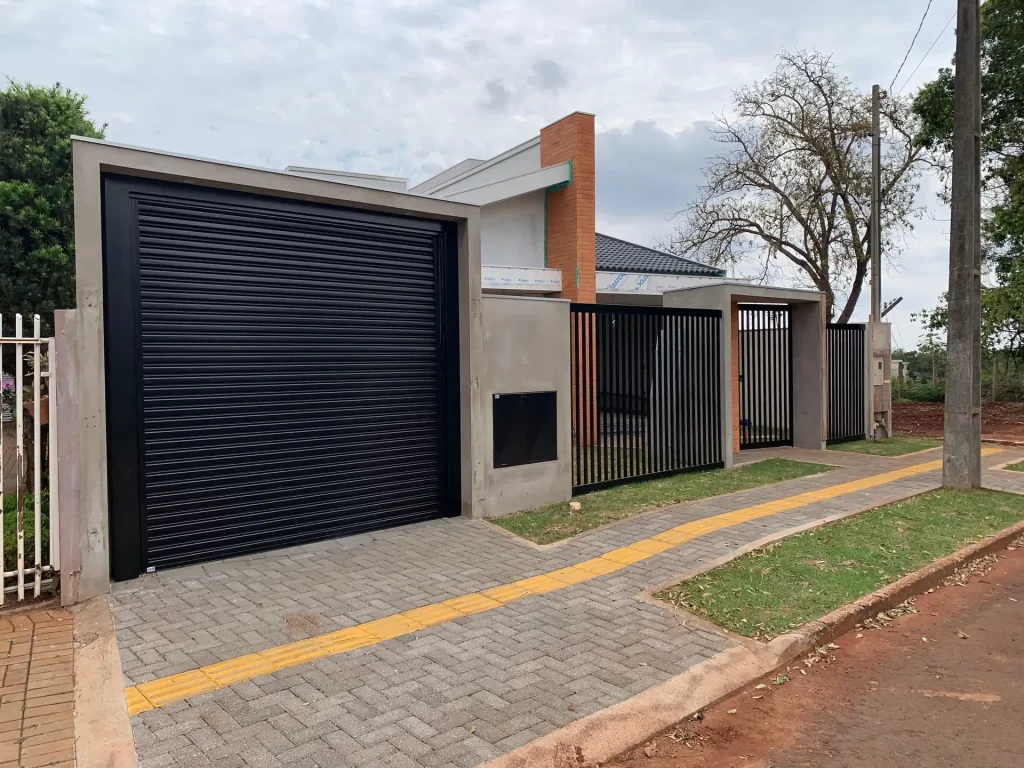 Residência entrada com portão automático preto e detalhe em tijolo, calçada concluída