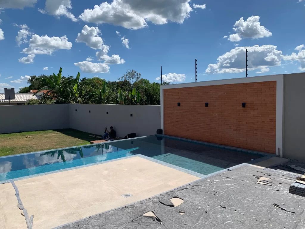 Área de lazer com piscina e parede revestida em tijolo aparente, obra concluída