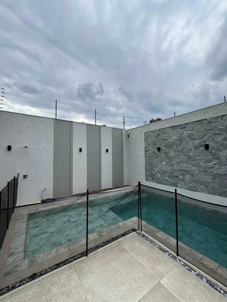 Piscina com revestimento em pedra cinza, deck e cerca de proteção, área concluída