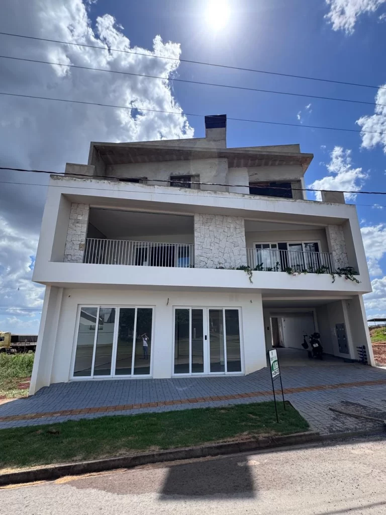 Edifício em fase de acabamento, fachada branca com revestimento em pedra na sacada e amplas portas de vidro no térreo, com pavimento superior ainda em estrutura de concreto aparente